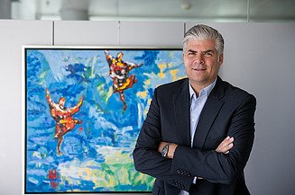 The new CEO of STRABAG SE, Stefan Kratochwill, stands with his arms folded and smiling in front of an art painting in the STRABAG building