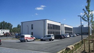 Foto von einem Neubau davor parken einige Firmenfahrzeuge, der Himmel ist blau