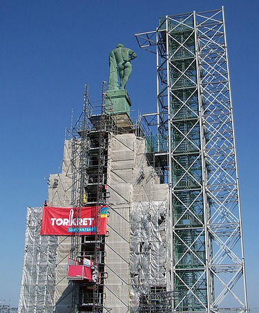  Foto von einer hochgebauten Statue, die auf einem Podest steht. Um das Podest ist ein Gerüst aufgebaut ist.
