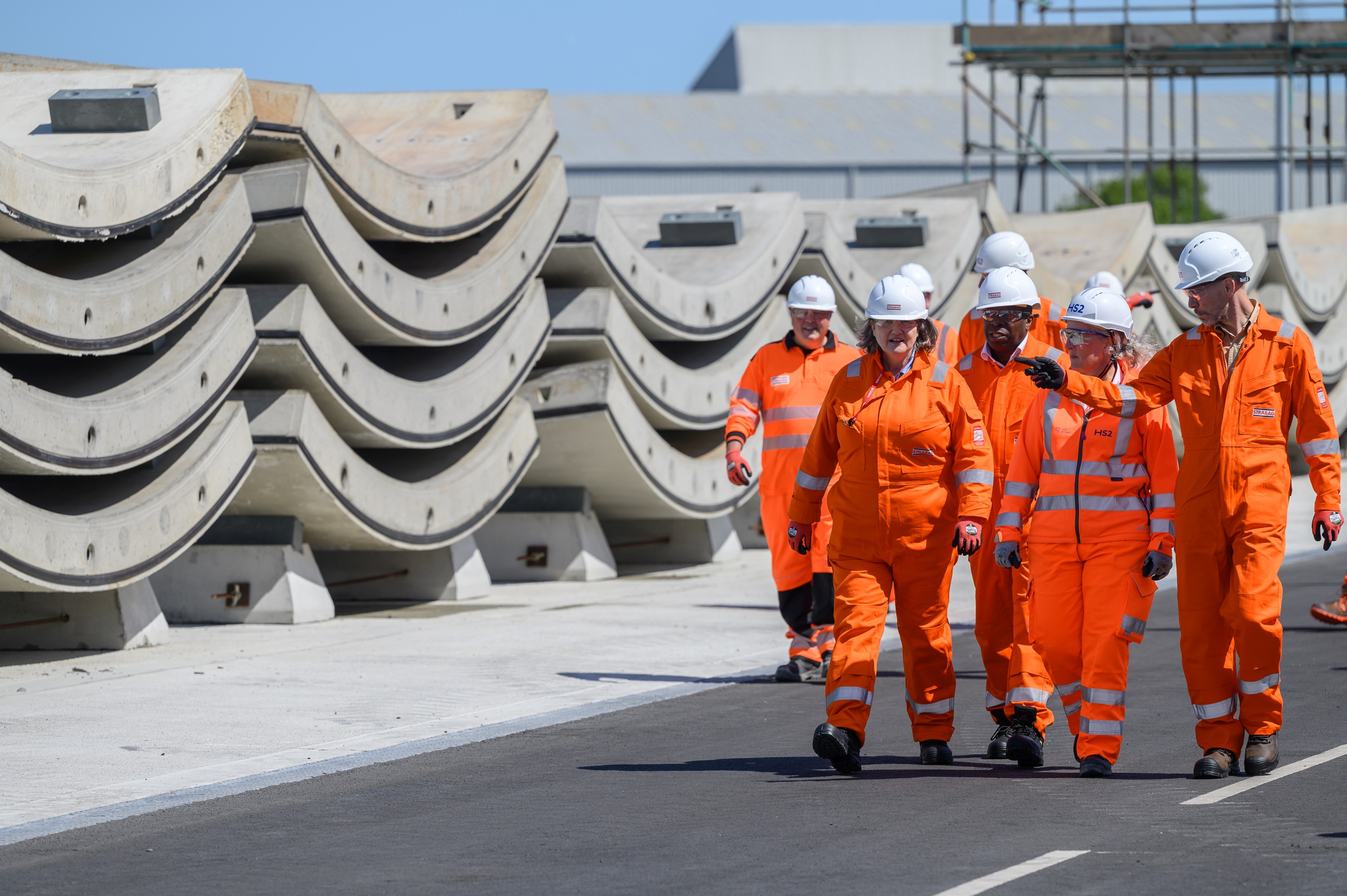 Photo of several people wearing hard hats and orange protective clothing walking next to precast concrete elements