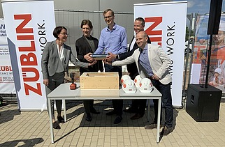 Foto von mehreren Personen, die eine Röhre halten bei der Grundsteinlegung.  