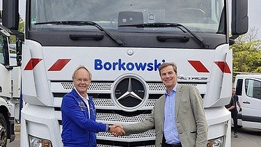 Foto von zwei männlichen Personen, die sich die Hand geben und vor einem LKW stehen mit der Aufschrift Borkowski