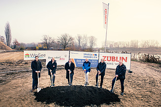 Foto von mehreren Männern, die einem Sparten in die Erde stecken. Sie schauen glücklich. 