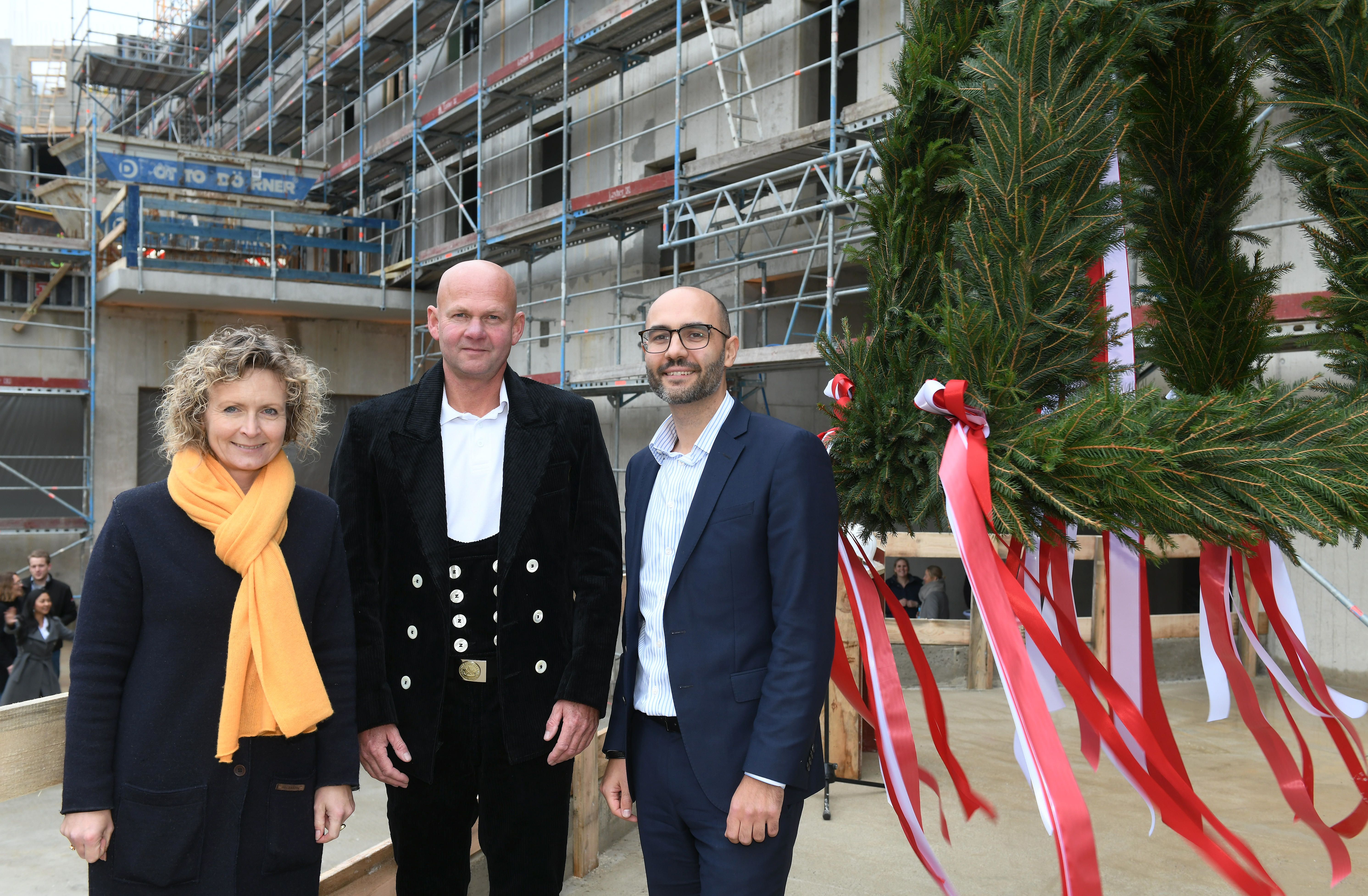 Foto von drei freundlich schauenden Personen auf einer Baustelle. Sie stehen vor dem Richtkranz.  