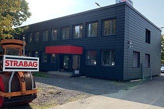 Foto eines schwarzen, einstöckigen Gebäudes, im Vordergrund eine STRABAG Bautafel