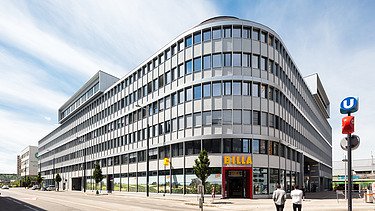 Photo shows a new office building complex, in front of it a street with two people