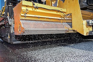 Foto einer gelben Asphaltbaumaschine bei der Arbeit