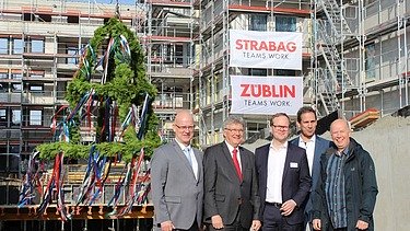 Foto von freundlich schauenden Männern auf einer Baustelle, beim hissen des Richtkranzes.  