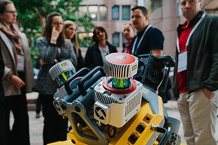 Photo shows an engine in the foreground, behind it some people are looking at it