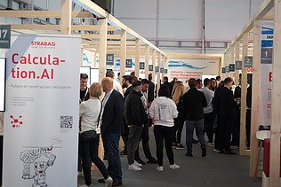 Photo of several people between exhibition stands, in the foreground on the left is a roll-up