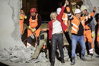 Foto von Personen in Schutzausrüstung und eine schick gekleidete Frau vor einem Tunnel. Die Frau und ein Mann reißen die Arme hoch und freuen sich.  