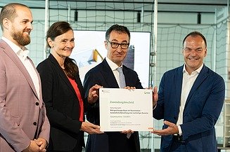 Nahaufnahme von vier Personen die schick gekleidet sind. Sie halten ein Zertifikat. 