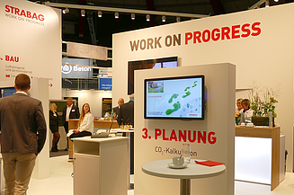 Foto eines Messestands, links geht eine Person vorbei, der Messestand ist mit Work on Progress beschriftet