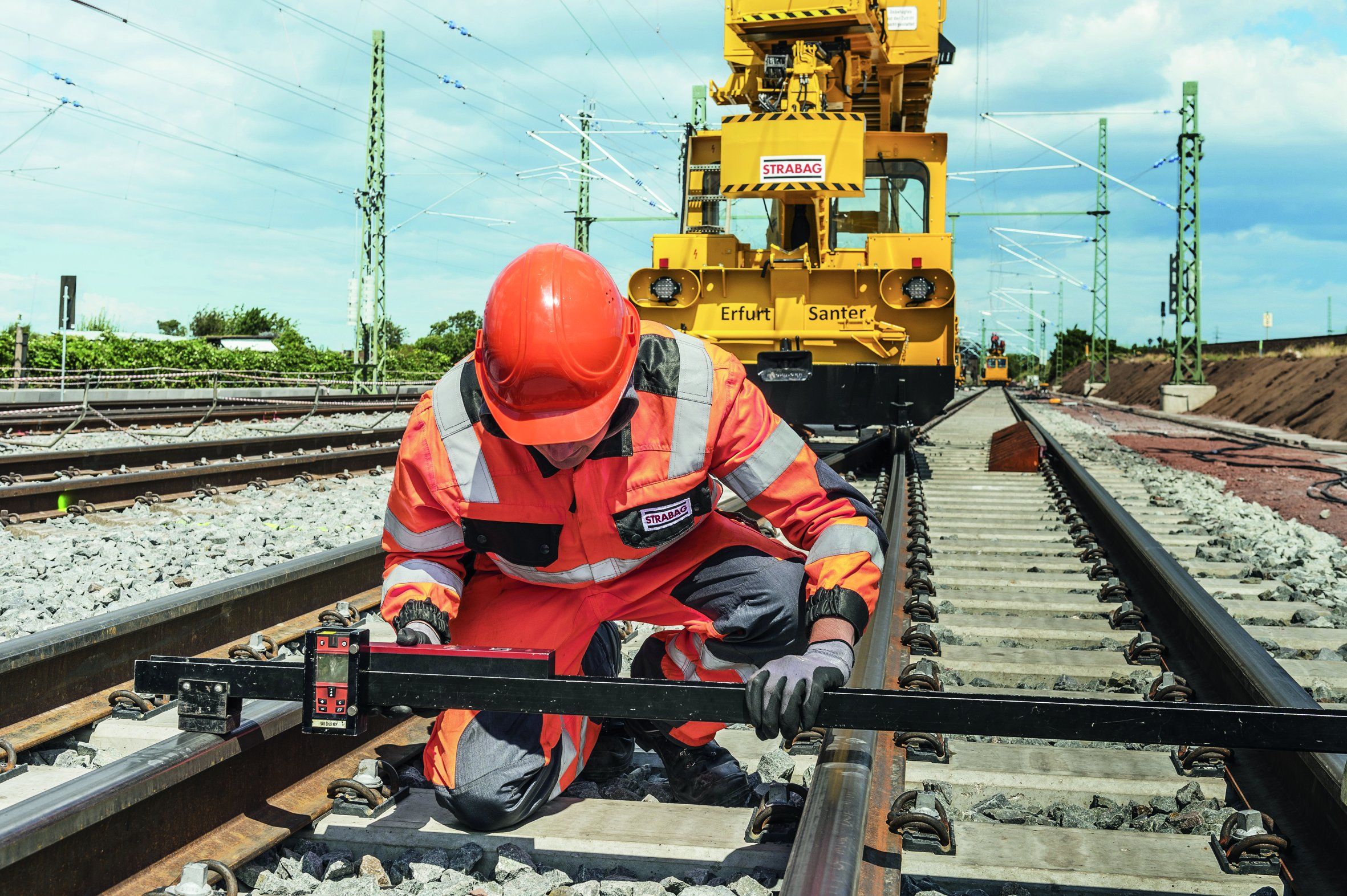 Photo of a rail worker in protective clothing, behind a yellow rail vehicle