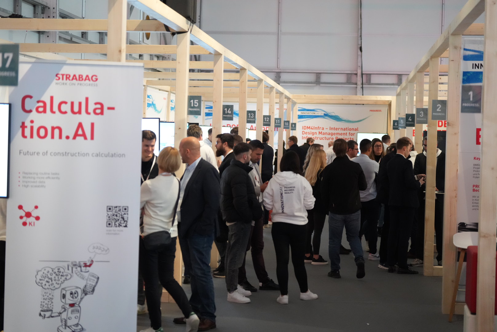 Photo of several people between exhibition stands, in the foreground on the left is a roll-up