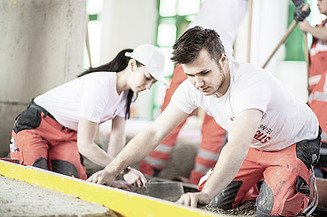 Das Bild zeigt zwei Personen in Arbeitskleidung bei der Arbeit
