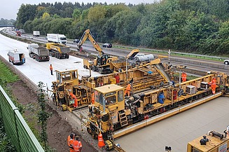 The picture shows a large concrete road construction machine in operation