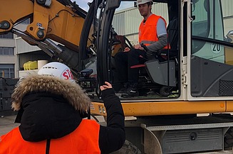 Foto von zwei Personen, die eine sitzt in einem Bagger, die andere steht davor