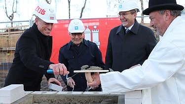 Foto von vier Männern bei der Grundsteinlegung für die Erweiterungsbau der Techniker Krankenkasse in Hamburg.