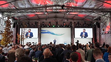 Photo of a ballroom with guests and a stage on which a presentation is running