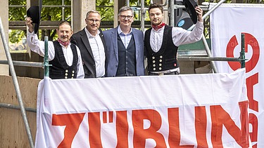 Foto von vier schick gekleideten Männern auf einem Gerüst. 