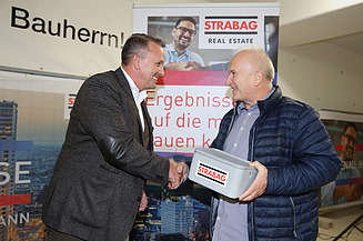 Foto von zwei Personen, die sich die rechte Hand schüttel, die Person rechts hält eine Geldschatulle in der linken hand