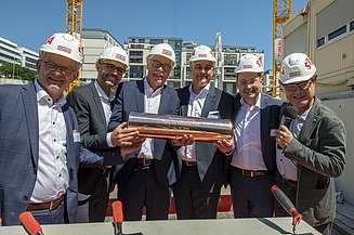 Foto von mehreren Männern auf einer Baustelle, die ein Gefäß in der Hand halten.  