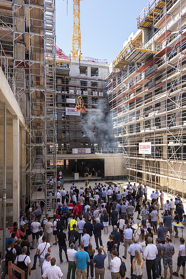 Foto von einer Baustelle, wo der Richtkranz aufgehangen wird. Viele Menschen schauen sich, dies an.      