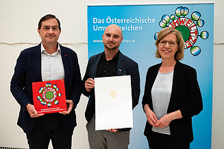 Foto von drei Personen, die beiden links halten jeweils eine Urkunde in den Händen