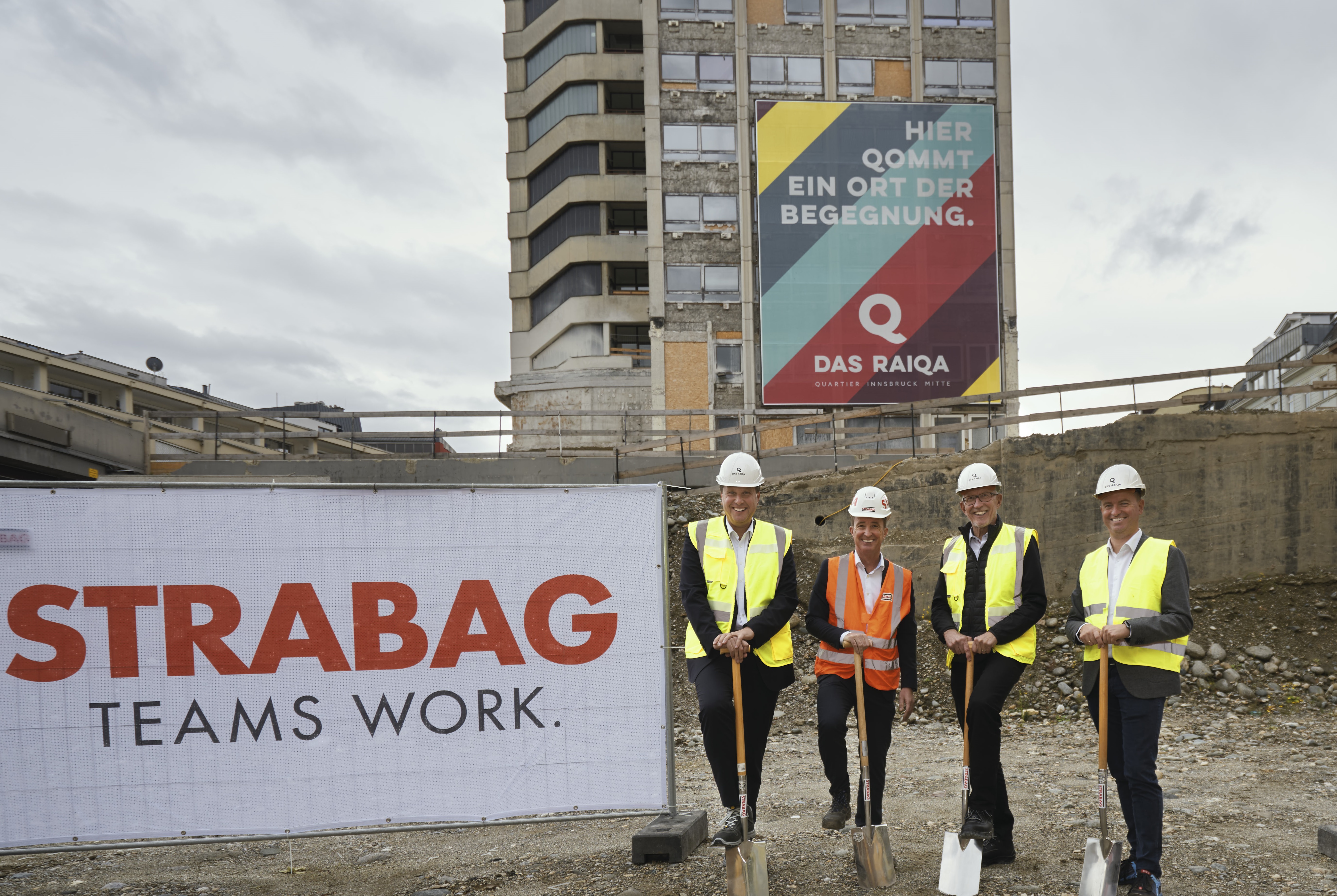 Foto von vier Personen stehen beim Spatenstich vor dem Raiqa Hochhaus, links ist ein STRABAG Transparent