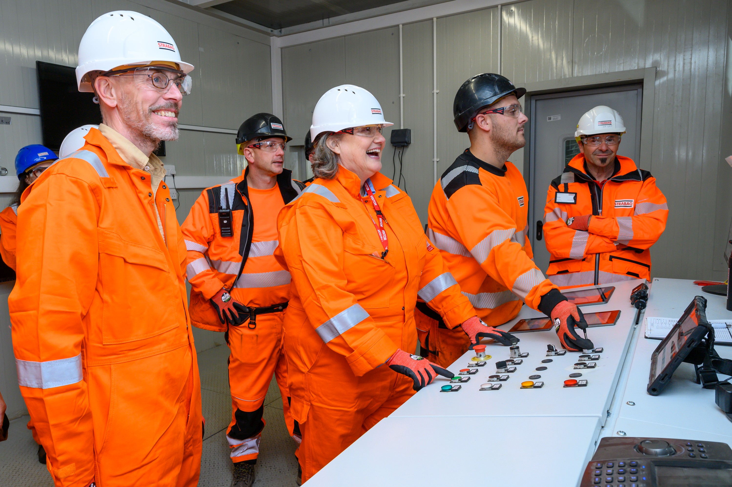 Photo of several people wearing hard hats and orange protective clothing standing at a control panel