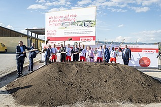 Das Bild zeigt mehrere Personen hinter einem Erdhaufen beim symbolischen Spatenstich