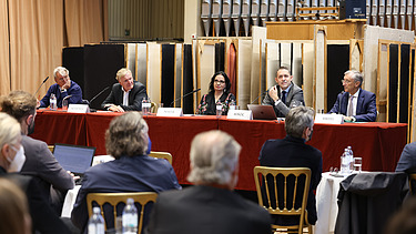 Foto einer Pressekonferenz, auf einer Bühne sitzen für Personen, die vor Publikaum vortragen
