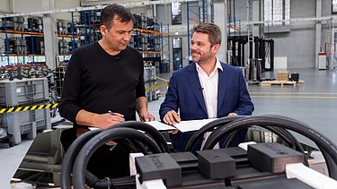 Foto von zwei Personen, die hinter einem Werktisch stehen, auf dem Batterien abgestellt sind