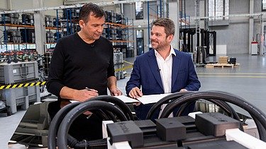 Photo of two people standing behind a workbench on which batteries are placed