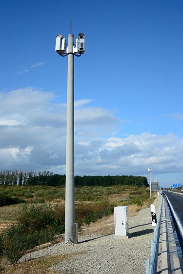 Foto eines Mastes mit einem technischen Gerät auf der Spitze, bei blauem Himmel