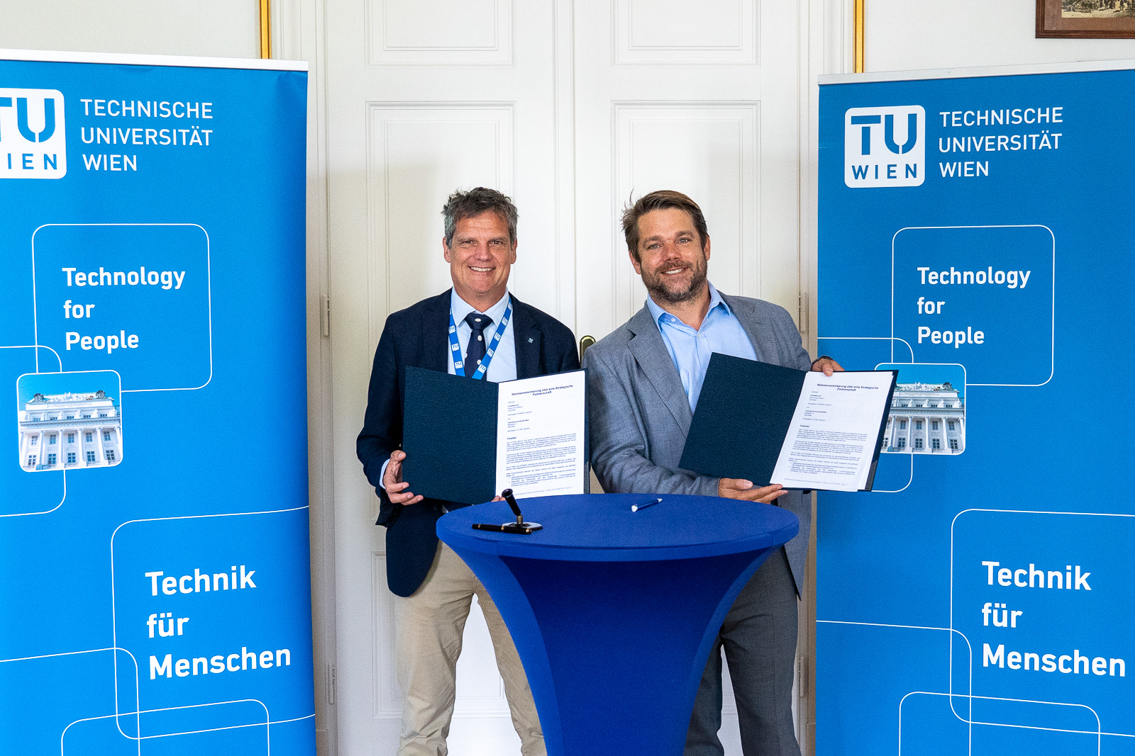 Foto von zwei Personen, die an einem Stehtisch stehen und Urkunden herzeigen