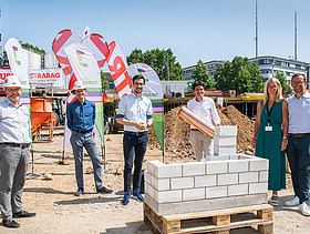 Foto von mehren Personen, die eine symbolische Grundsteinlegung durchführen. 