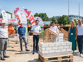 Foto von mehren Personen, die eine symbolische Grundsteinlegung durchführen. 