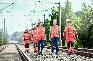 Foto von fünf Personen, die zwischen zwei Bahngleisen mit Oberleitungen gehen