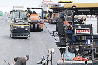Foto von mehreren Straßenbaumaschinen und einem Arbeiter mit einer Schaufel