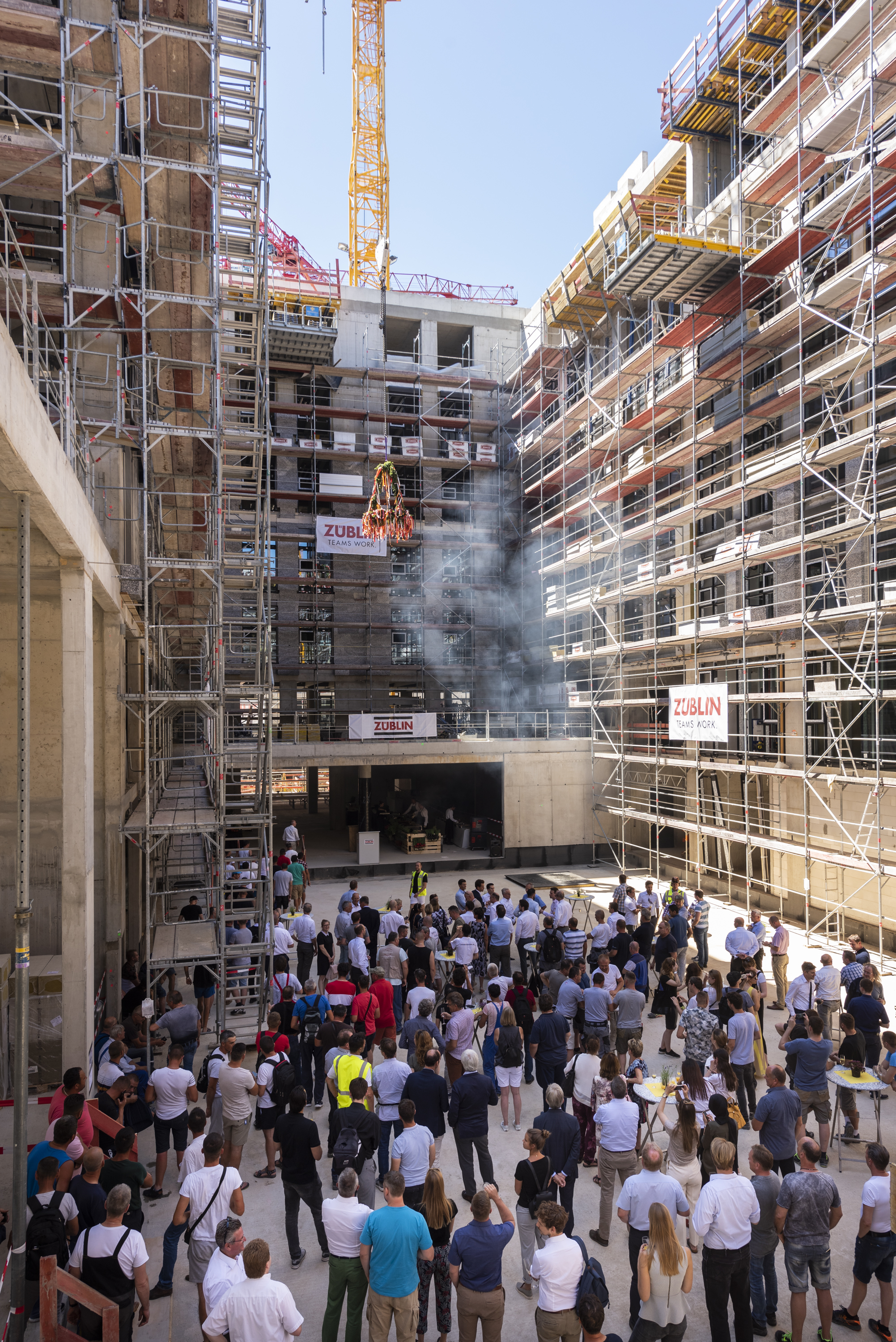 Foto von einer Baustelle, wo der Richtkranz aufgehangen wird. Viele Menschen schauen sich, dies an.      