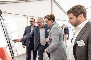 Foto von vier Personen, die eine Bautafel betrachten, die zweite Person von links zeigt darauf