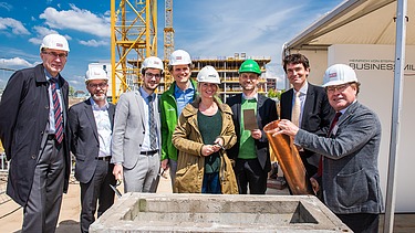 Foto von einer Frau und mehreren Männern auf einer Baustelle, bei symbolischer Grundsein für das JobRad-Firmenzentrale. Ein Mann hält eine Röhre. 