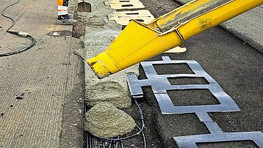 Foto von zwei Straßenbauarbeitern mit einer gelben Maschine