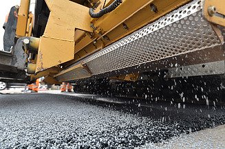 Foto einer Detailansicht einer gelben Asphaltiermaschine bei der Arbeit
