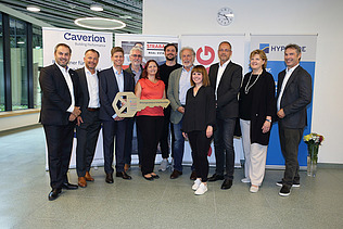 Foto von mehreren Personen bei der Schlüsselübergabe, sie stehen vor zwei Roll-ups