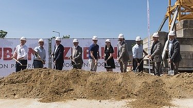 Foto von mehreren Personen die mit einem Sparten Erde schaufeln.   