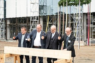 Foto von vier Männern die einen Nagel in ein Holzbrett hauen.  