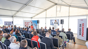 A man stands on a stage. The audience sits in front of the stage